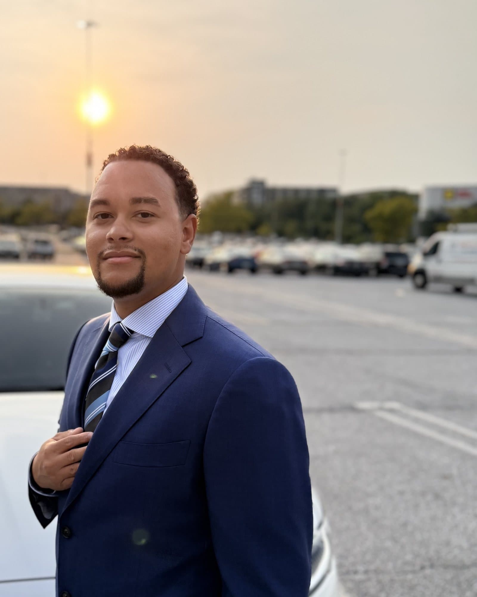 Justin Brown in a navy suit at sunset, hand on his chest
